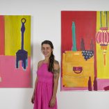 Natasha Radovicz Schaidt pictured between two paintings entitled Clownin' and Beers with Billie.