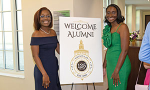 two alumni showing off an alumni event sign