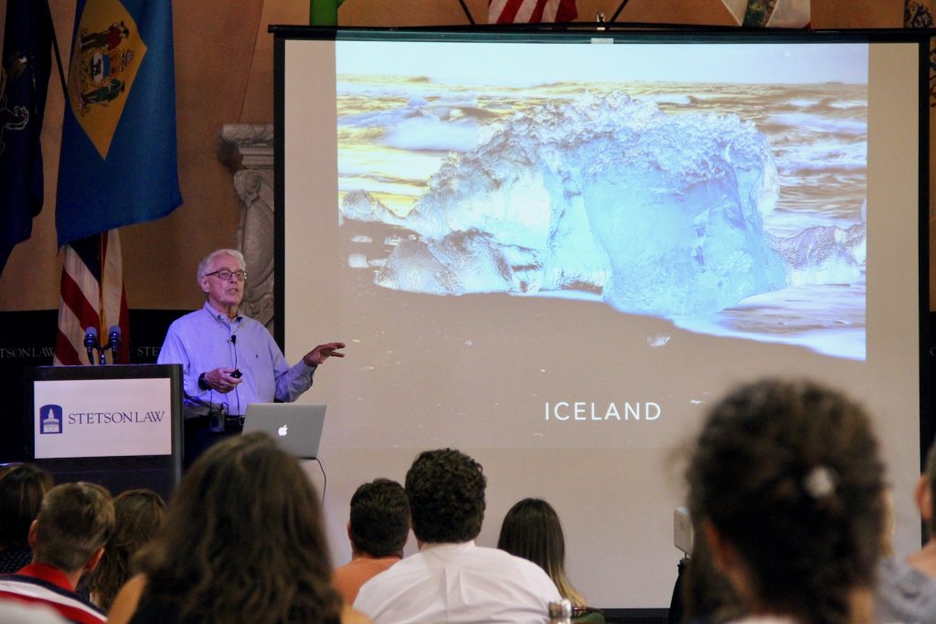 A man stands at a podium in front of an aerial image of Iceland.