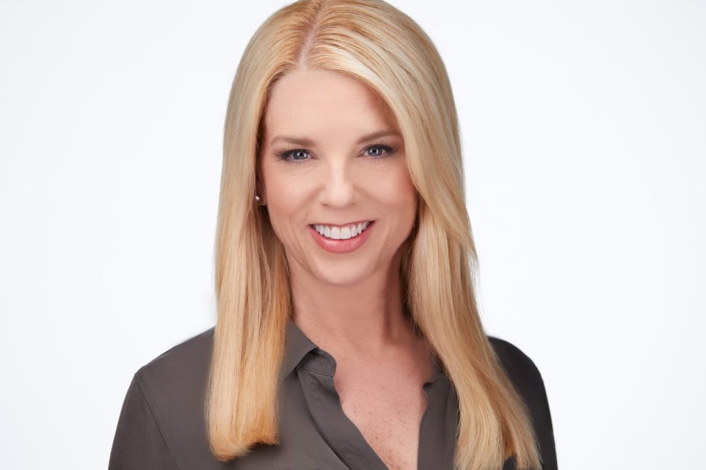A headshot of a woman with long blonde hair. She is smiling.