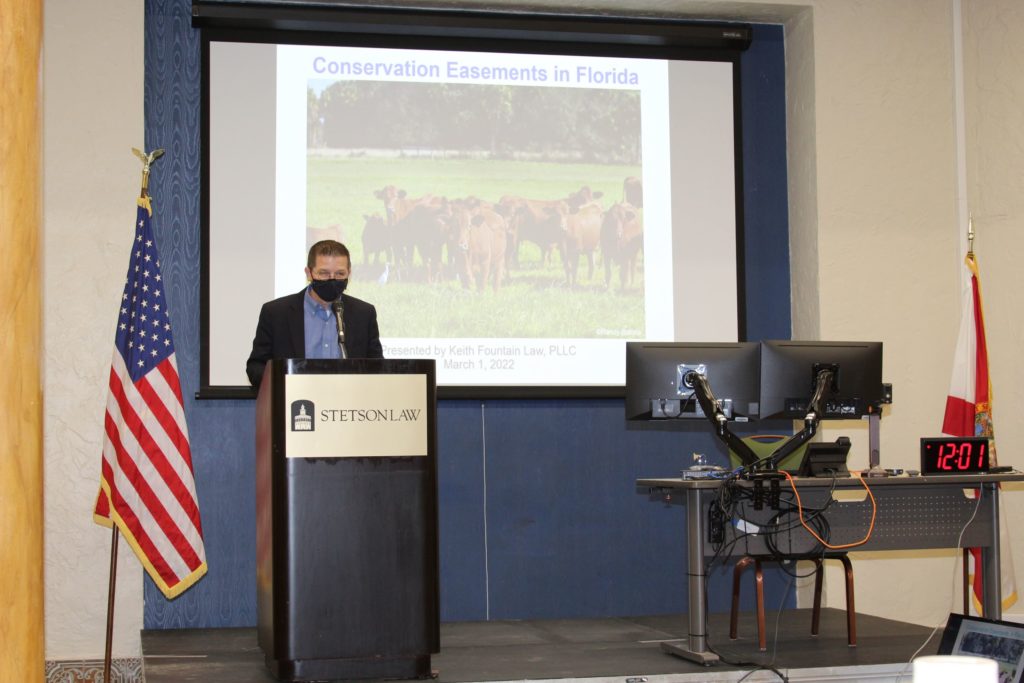 Professor Royal Gardner stands in front of a screen featuring a herd of cows