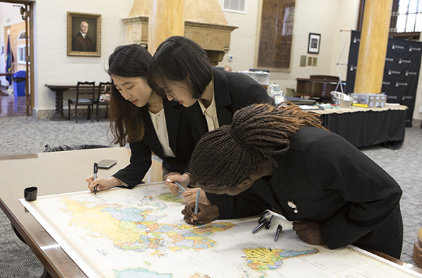 Three women sign a map of the world using Sharpie markers.