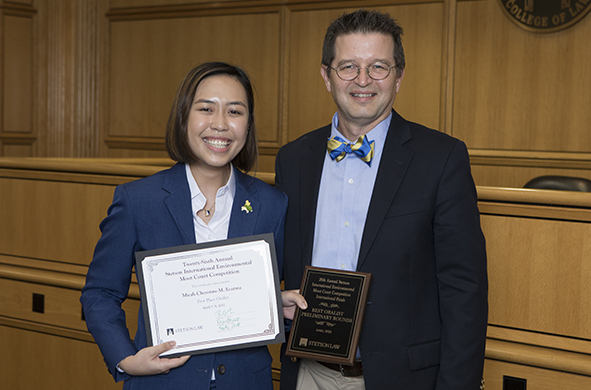 Micah Cheyenne Ecarma of the University of the Philippines College of Law holds two award plaques next to Professor Royal Gardner.