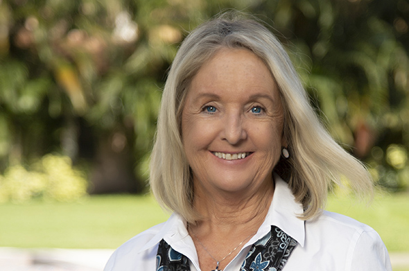 A headshot of Professor Roberta Flowers, who is smiling before a backdrop of greenery.