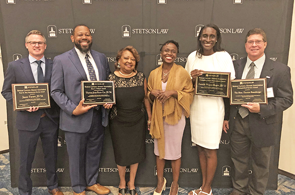 Six people pose and hold their awards in front of a Stetson Law backdrop.