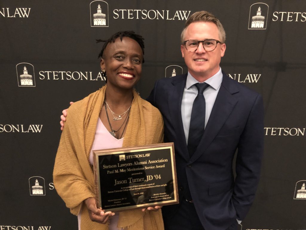 Dean Michele Alexandre and alumnus Jason Turner pose with Turner's award plaque.