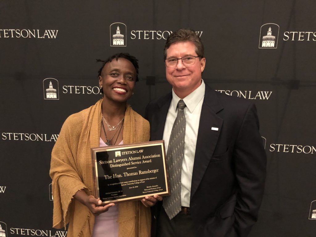 Dean Michele Alexandre and The Hon. Thomas Ramsberger pose with a plaque honoring Ramsberger's service.