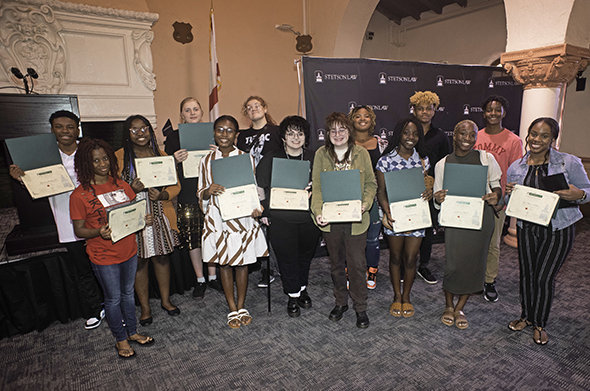 A group of young students holds up diplomas in Stetson Law's Great Hall.