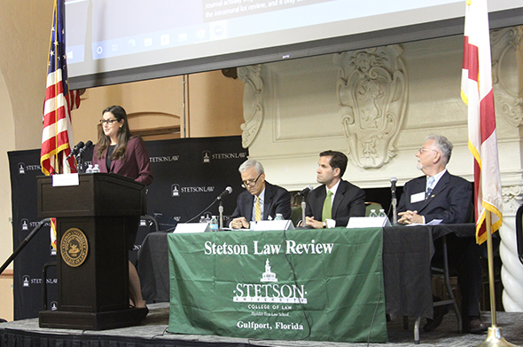 A law student stands at a podium to introduce several judges on a panel.