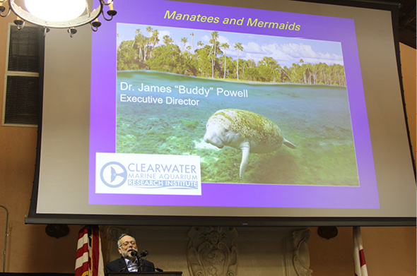 A man speaks at a podium with a manatee on display in the background.