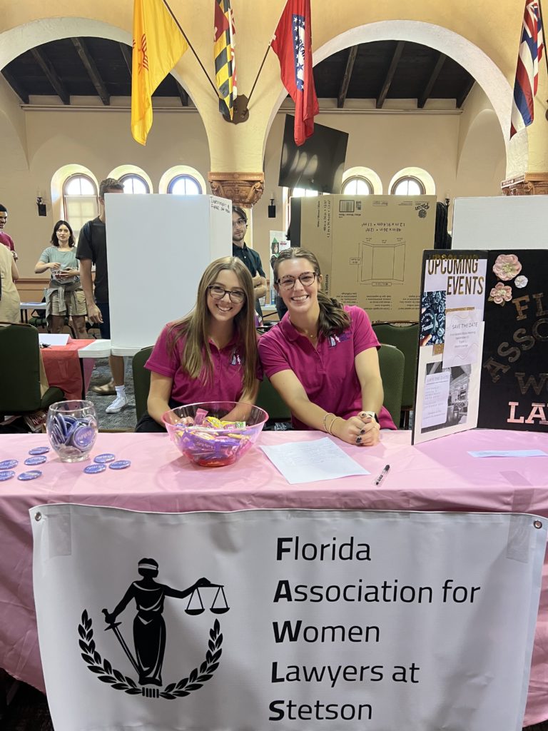 Two female law students sit at a table promoting their organization at an event in the Great Hall