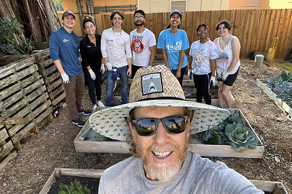 A professor and several students pose for a selfie in front of a garden.