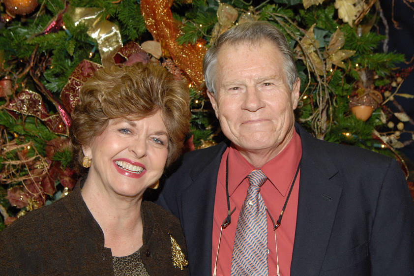 A picture of an elder couple standing in front of a Christmas tree.
