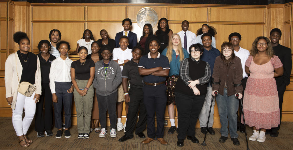 A group of high-school students poses in front of the judge's bench in a practice courtroom.