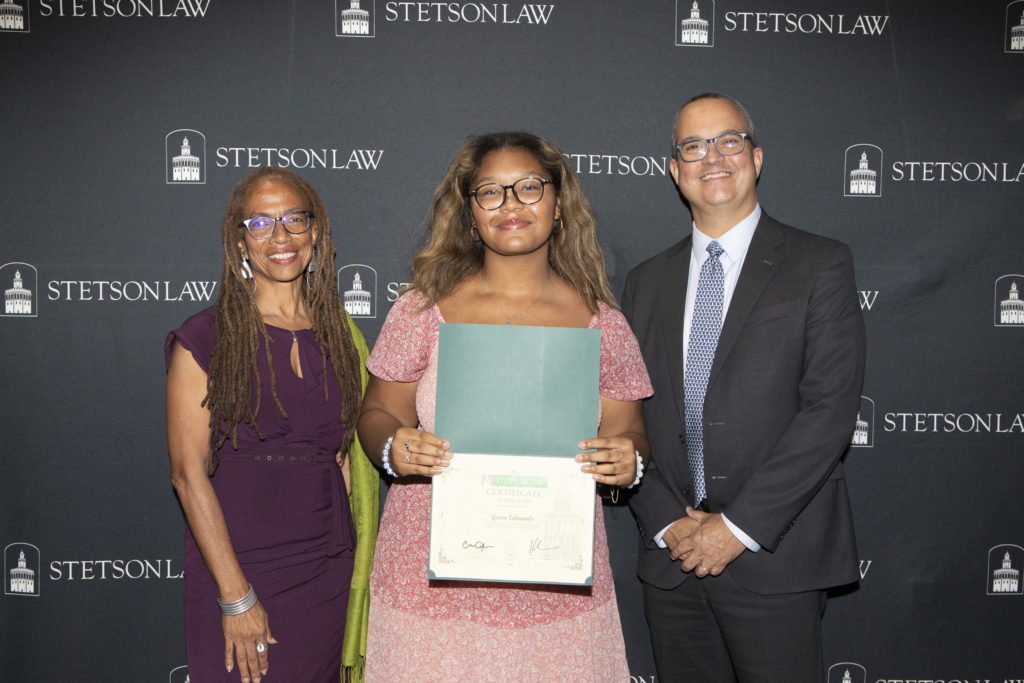 Professors pose with a student, who holds a certificate.