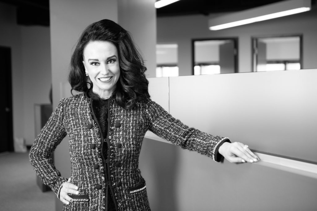 A black-and-white photograph of a woman named Brittany Maxey-Fisher smiling in an office.