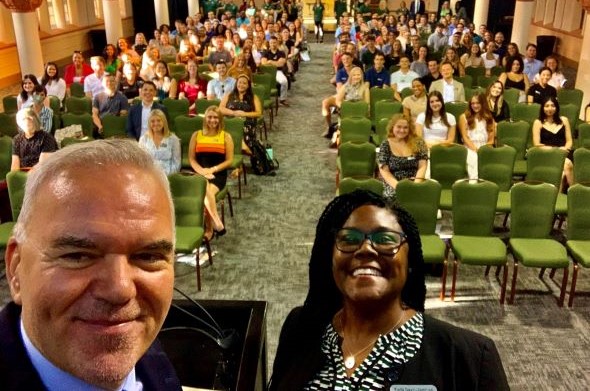 Admissions office leaders take a selfie from behind a podium with incoming law students in the background in the Great Hall.