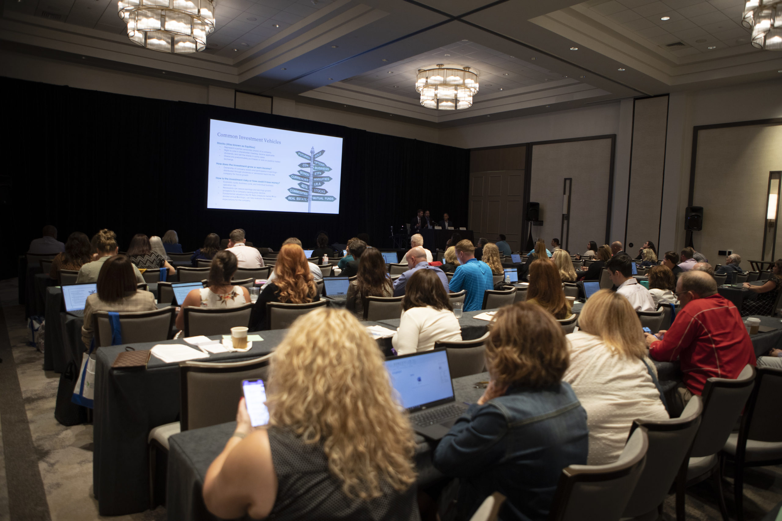 Viewed from the back of the room, dozens of attendees watch a presentation at a large conference.