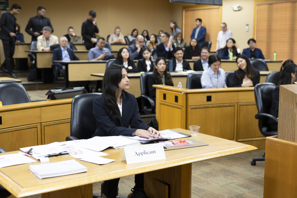 A woman sits in the foreground in a courtroom during a mock trial.