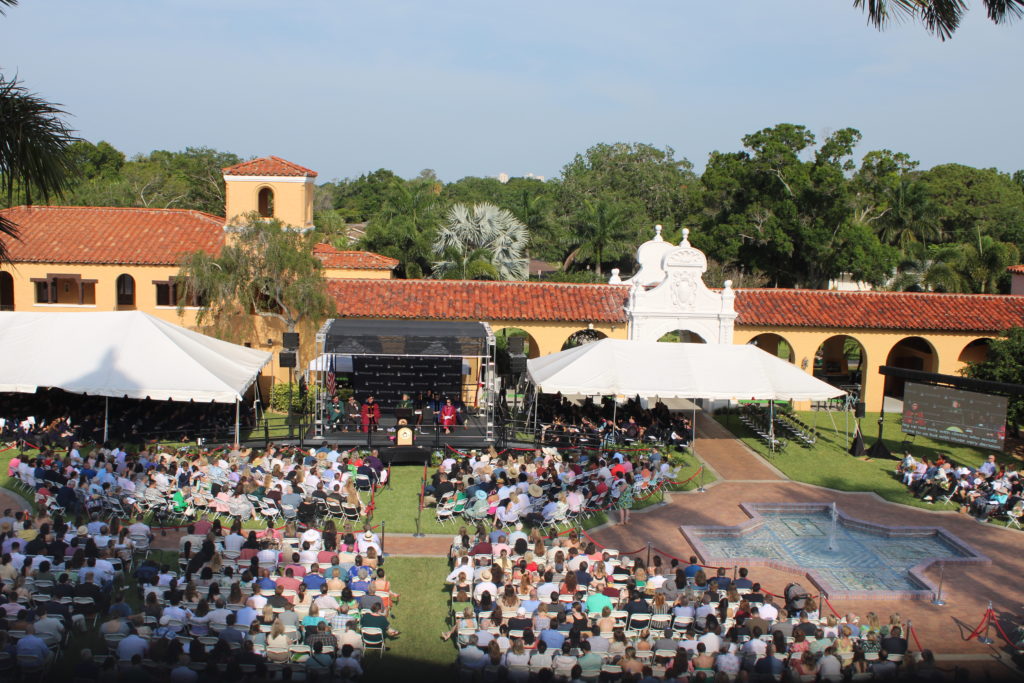 An aerial shot of a large courtyard and stage where hundreds of people are gathered for a graduation ceremony.