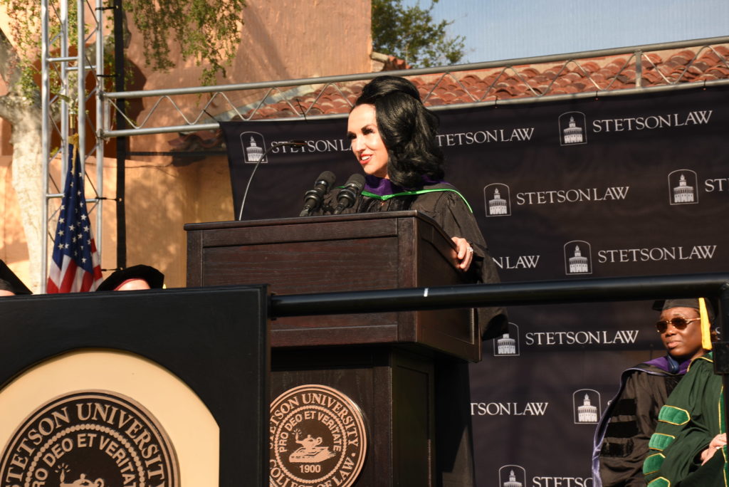 A woman with dark hair speaks at a podium during a graduation ceremony