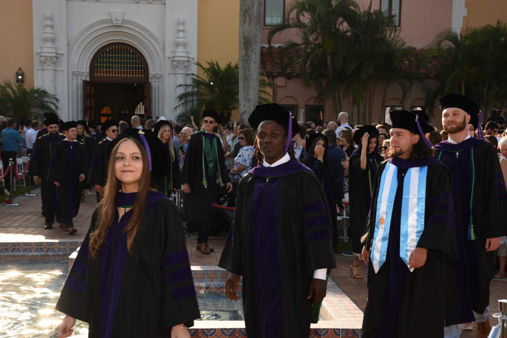 Three young people in graduation caps and gowns stand in a courtyard right after graduating from law school.