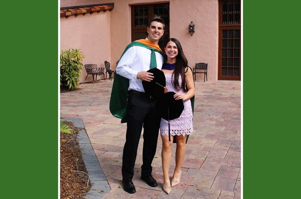 A young man and woman stand in a courtyard holding graduation garb.
