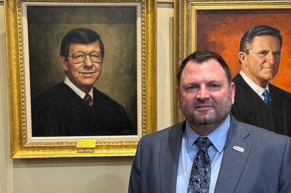 A man in a suit stands next to a portrait of a judge who is his former mentor.