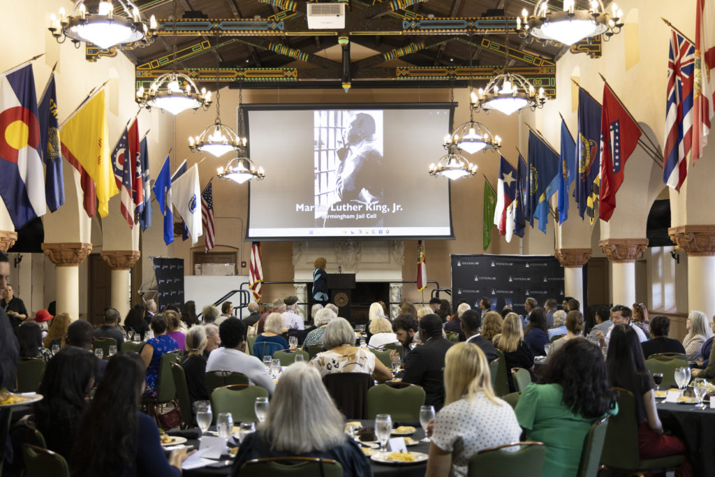 The back of the room as an audience watches a video. Footage of Dr. Martin Luther King, Jr. is on the screen.