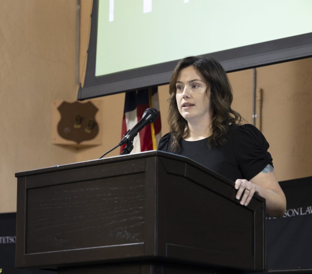 A woman in a black dress speaks at a podium.