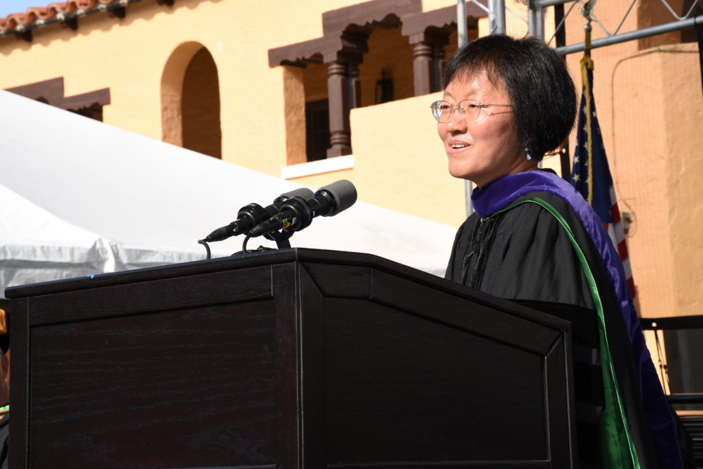 A woman with short dark hair speaks at a podium during graduation.
