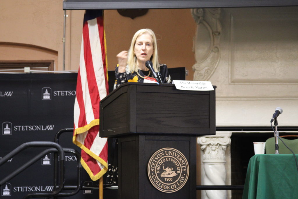 A woman with blonde hair makes a fist as she speaks at a podium.