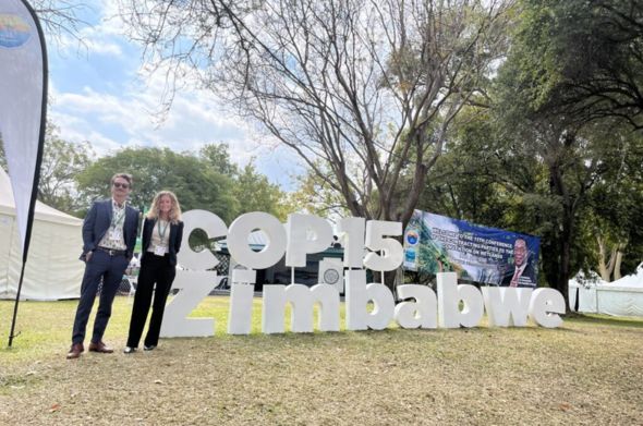 Two students stand by a sign advertising COP 15 Zimbabwe.