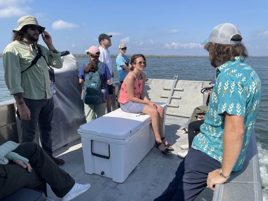 Several students and a boat captain sit on a boat in open water.