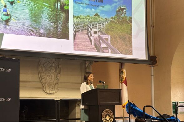 A woman speaks at a podium in Stetson Law's Great Hall. Photos of Florida's State Parks are projected behind her.