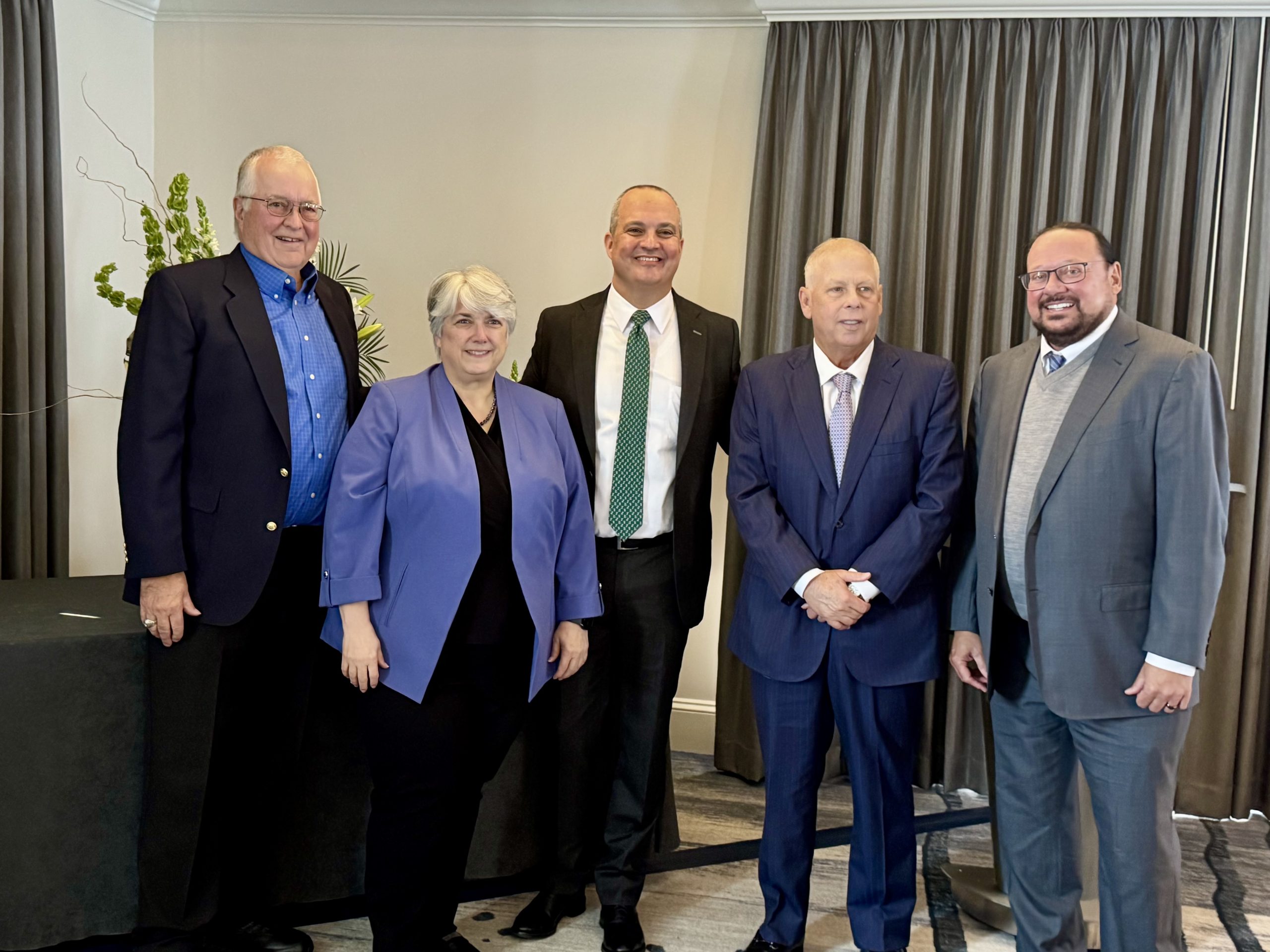 Five people stand in a row and smile for the camera.