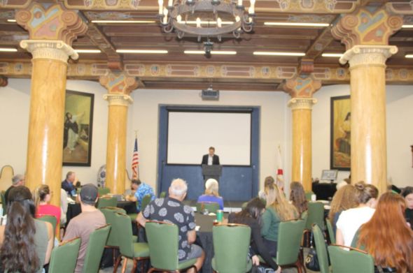 A man speaks at a podium in a room with marble columns.