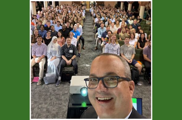 Dean D. Benjamin Barros smiles for a selfie in front of a class of students at orientation in the Great Hall.