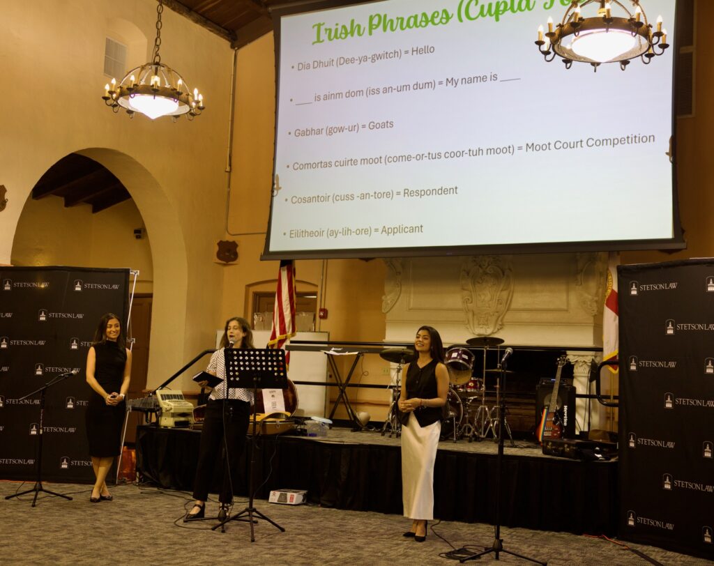 A group of students stand on a stage in front of a screen explaining their traditions.