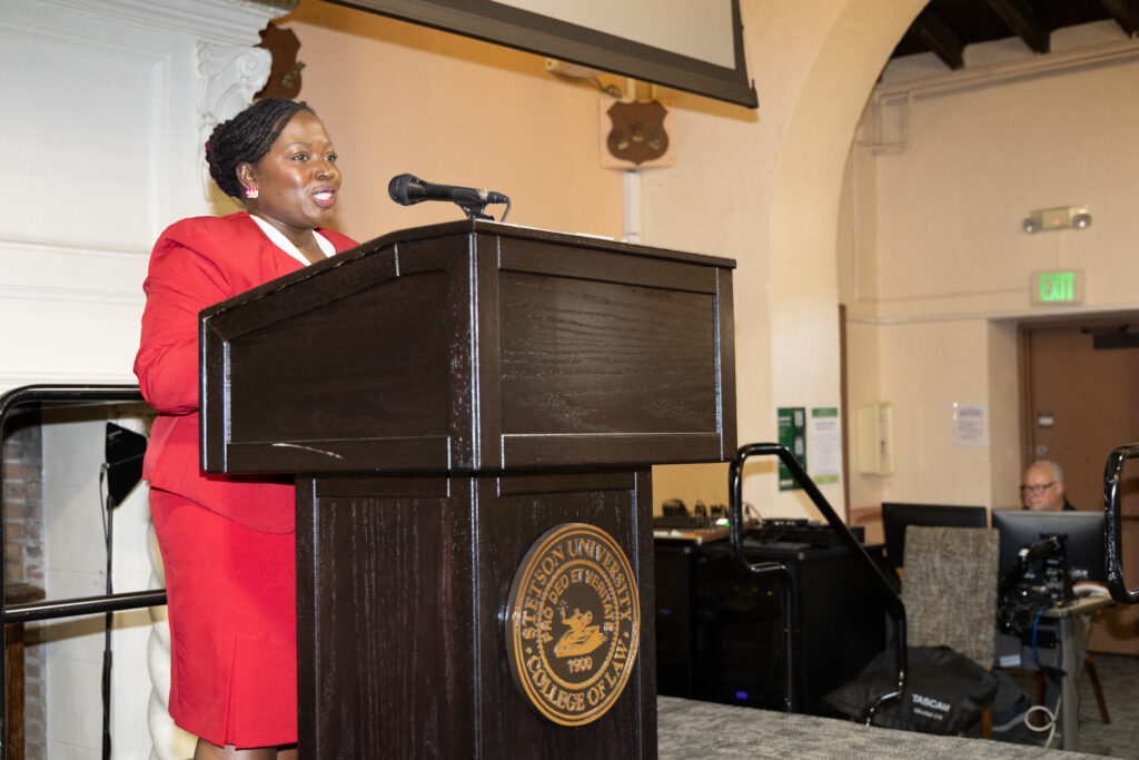 A woman with an updo wearing a red suit speaks at a podium.