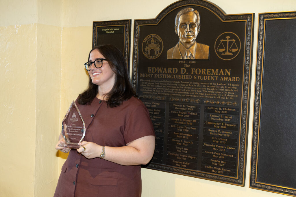 A woman wearing a brown dress stands in front of a plaque featuring the likeness of Edward D. Foreman.
