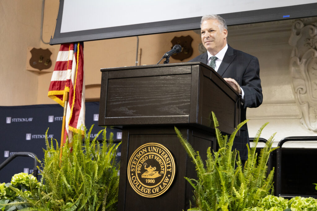 A man wearing a suit speaks at a podium featuring the Stetson University College of Law logo.