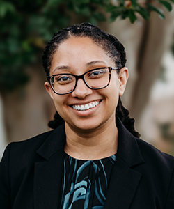 A young woman with glasses smiles.