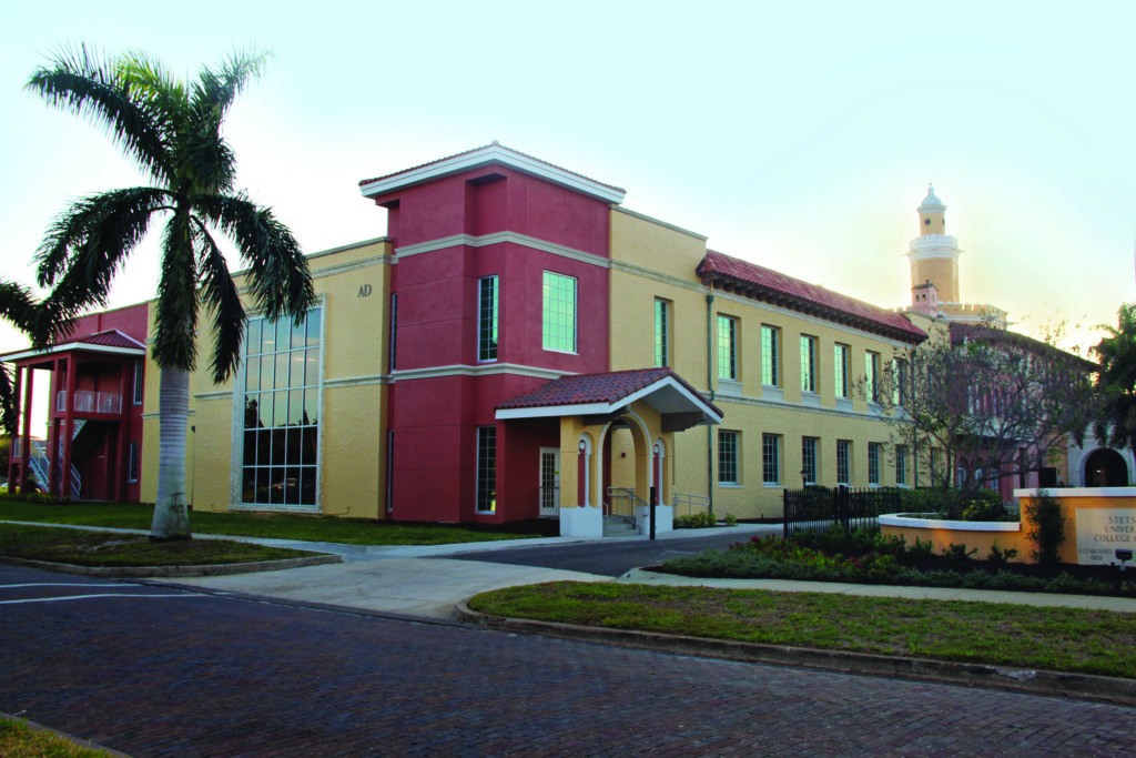 An exterior shot of a red and beige building with a palm tree in the foreground.