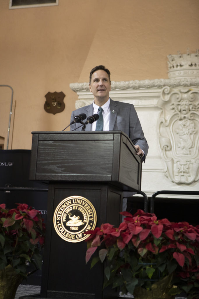 A man speaking at a podium with poinsettia plants in the foreground.