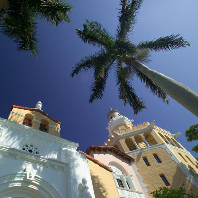 exterior shot of buildings and palm trees, looking up at blue sky.