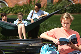 Student seated on bench, reading a book