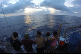 Students at sea stand at ship's railing and look out over the ocean