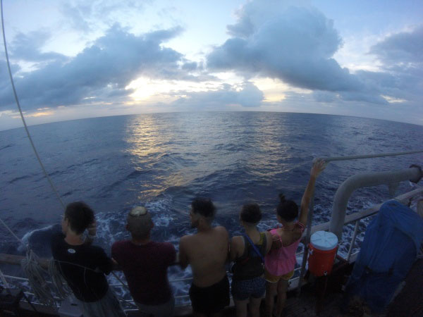 Students at sea stand at ship's railing and look out over the ocean.
