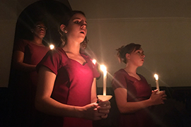 Women's Chorale, dressed in gowns and holding candles